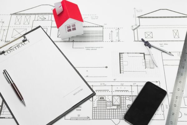 Ghar Ka Naksha Kaise Banaya Jata Hai – Architectural blueprint, house model, contract paper, scale, and smartphone placed on a desk, representing proper design and planning.