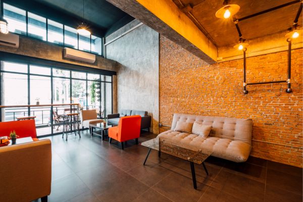 A modern industrial interior design space featuring exposed brick walls, metal lighting fixtures, high ceilings, and large glass windows. 